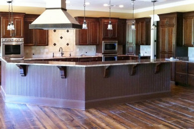 Inspiration for a huge timeless l-shaped medium tone wood floor open concept kitchen remodel in New Orleans with an undermount sink, raised-panel cabinets, dark wood cabinets, granite countertops, stone tile backsplash, stainless steel appliances and an island