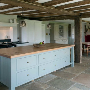 Photo of a country kitchen/diner in Sussex with shaker cabinets, white cabinets, black appliances, an island, multi-coloured floors and black worktops.