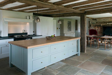 Photo of a country kitchen/diner in Sussex with shaker cabinets, white cabinets, black appliances, an island, multi-coloured floors and black worktops.
