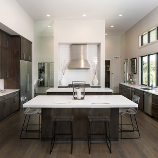 Photo of a large contemporary single-wall open plan kitchen in Wichita with an undermount sink, flat-panel cabinets, dark wood cabinets, white splashback, stainless steel appliances, dark hardwood floors, multiple islands, solid surface benchtops and porcelain splashback.