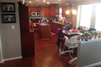 シンシナティにあるおしゃれなキッチン (レイズドパネル扉のキャビネット、中間色木目調キャビネット、御影石カウンター、ベージュキッチンパネル、シルバーの調理設備、無垢フローリング) の写真