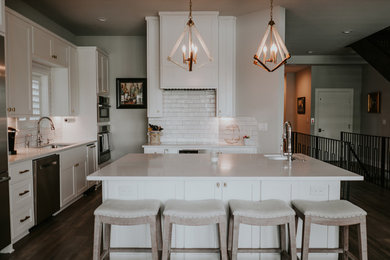 Inspiration for a mid-sized modern l-shaped dark wood floor and brown floor eat-in kitchen remodel in Austin with a single-bowl sink, shaker cabinets, white cabinets, quartz countertops, white backsplash, ceramic backsplash, stainless steel appliances, an island and white countertops
