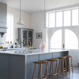Traditional galley kitchen/diner in Other with a belfast sink, recessed-panel cabinets, grey cabinets, white splashback, an island, grey floors and white worktops.