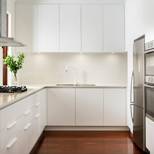 Contemporary u-shaped separate kitchen in Perth with a drop-in sink, flat-panel cabinets, white cabinets, white splashback, subway tile splashback, dark hardwood floors, no island, brown floor and white benchtop.