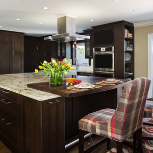 Mid-sized transitional l-shaped eat-in kitchen in Miami with a farmhouse sink, shaker cabinets, dark wood cabinets, limestone benchtops, white splashback, ceramic splashback, stainless steel appliances, medium hardwood floors and with island.
