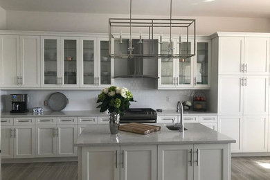Exempel på ett stort klassiskt grå linjärt grått kök och matrum, med luckor med infälld panel, vita skåp, bänkskiva i kvarts, vitt stänkskydd, stänkskydd i porslinskakel, rostfria vitvaror, klinkergolv i porslin, en köksö och brunt golv