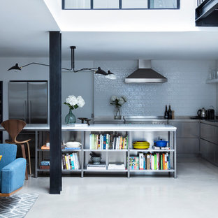 Inspiration for a mid-sized industrial galley open plan kitchen in London with an integrated sink, flat-panel cabinets, stainless steel cabinets, stainless steel benchtops, white splashback, ceramic splashback, stainless steel appliances, concrete floors and with island.