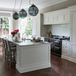 This is an example of a large traditional galley open plan kitchen in London with a drop-in sink, shaker cabinets, yellow cabinets, quartzite benchtops, black appliances, dark hardwood floors, multiple islands and yellow benchtop.