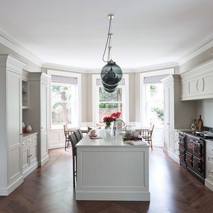 Large classic galley kitchen/diner in London with shaker cabinets, quartz worktops, black appliances, dark hardwood flooring, white cabinets, an island, brown floors and white worktops.