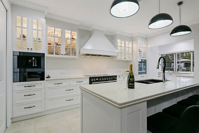 Photo of a large classic galley open plan kitchen in Brisbane with a submerged sink, shaker cabinets, white cabinets, engineered stone countertops, white splashback, porcelain splashback, black appliances, porcelain flooring and an island.