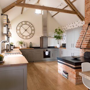 Design ideas for a medium sized rural u-shaped open plan kitchen in Other with a belfast sink, recessed-panel cabinets, grey cabinets, wood worktops, beige floors, brown worktops, integrated appliances, medium hardwood flooring and no island.