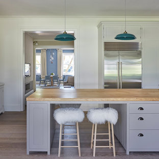 Large classic kitchen in London with a submerged sink, shaker cabinets, grey cabinets, an island, wood worktops, stainless steel appliances and light hardwood flooring.