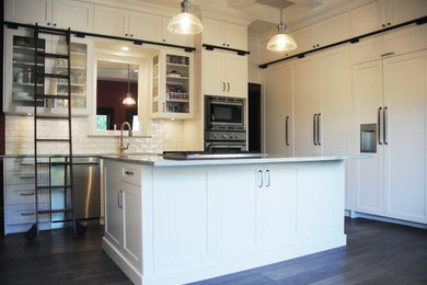 Photo of a large traditional kitchen/diner in Vancouver with a submerged sink, shaker cabinets, white cabinets, quartz worktops, white splashback, ceramic splashback, stainless steel appliances, light hardwood flooring, an island and brown floors.