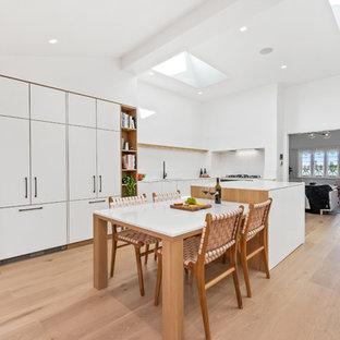 Inspiration for a scandinavian l-shaped kitchen in Perth with flat-panel cabinets, white cabinets, white splashback, light hardwood floors, beige floor, white benchtop and panelled appliances.