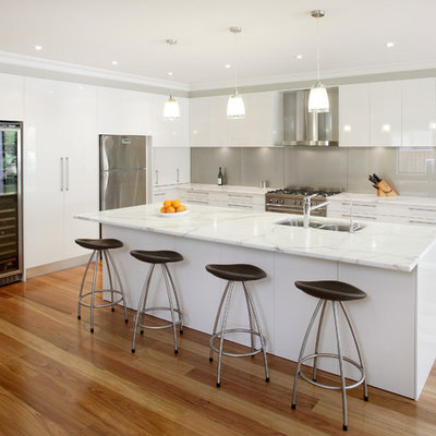 Inspiration for a mid-sized contemporary l-shaped medium tone wood floor kitchen remodel in Sydney with stainless steel appliances, an undermount sink, white cabinets, marble countertops, metallic backsplash, glass sheet backsplash and an island