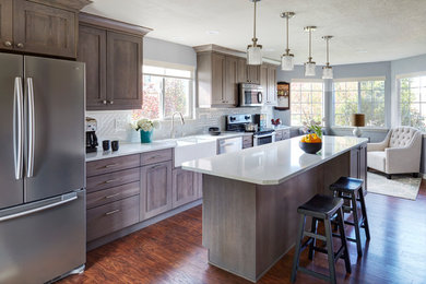 Mid-sized transitional single-wall dark wood floor eat-in kitchen photo in Denver with a farmhouse sink, shaker cabinets, gray cabinets, quartz countertops, white backsplash, ceramic backsplash, stainless steel appliances and an island
