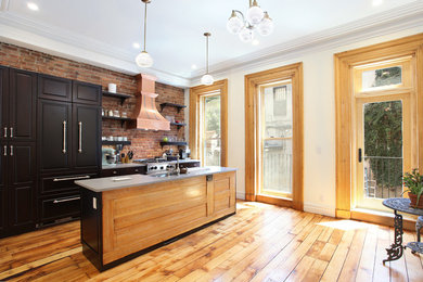 Inspiration for a mid-sized industrial galley medium tone wood floor open concept kitchen remodel in New York with raised-panel cabinets, black cabinets, an island, solid surface countertops, red backsplash, brick backsplash, stainless steel appliances and a farmhouse sink