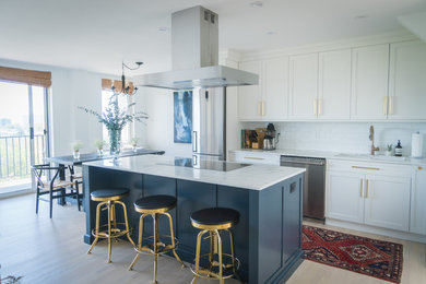 Imagen de cocina comedor moderna de tamaño medio con fregadero bajoencimera, armarios estilo shaker, puertas de armario blancas, encimera de mármol, salpicadero blanco, salpicadero de azulejos tipo metro, electrodomésticos de acero inoxidable, suelo de madera clara, una isla y suelo marrón