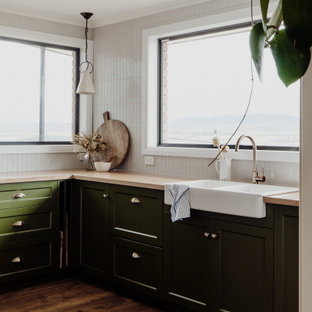 Design ideas for a mid-sized transitional l-shaped kitchen in Hobart with a farmhouse sink, shaker cabinets, green cabinets, wood benchtops, white splashback, cement tile splashback, stainless steel appliances, medium hardwood floors, no island, brown floor and beige benchtop.