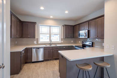 Mid-sized trendy u-shaped light wood floor eat-in kitchen photo in Other with a double-bowl sink, raised-panel cabinets, medium tone wood cabinets, quartz countertops, beige backsplash, subway tile backsplash, stainless steel appliances and no island