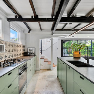 Design ideas for a large transitional galley open plan kitchen in Brisbane with a double-bowl sink, flat-panel cabinets, green cabinets, quartz benchtops, ceramic splashback, concrete floors, with island, multi-coloured splashback, black appliances, beige floor, black benchtop and exposed beam.