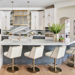 Photo of a mid-sized transitional l-shaped open plan kitchen in Austin with shaker cabinets, multi-coloured splashback, stainless steel appliances, light hardwood floors, multiple islands, a farmhouse sink, grey cabinets, quartzite benchtops, marble splashback, grey floor and blue benchtop.