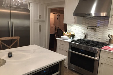 Foto de cocina tradicional renovada de tamaño medio cerrada con armarios estilo shaker, electrodomésticos de acero inoxidable, una isla, encimeras blancas y suelo beige