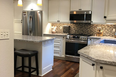 Mid-sized elegant galley dark wood floor and multicolored floor eat-in kitchen photo in Portland with an undermount sink, raised-panel cabinets, white cabinets, granite countertops, multicolored backsplash, glass tile backsplash, stainless steel appliances, an island and multicolored countertops