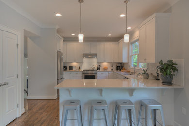 Medium sized traditional l-shaped enclosed kitchen in DC Metro with a submerged sink, shaker cabinets, white cabinets, composite countertops, white splashback, metro tiled splashback, stainless steel appliances, medium hardwood flooring and a breakfast bar.