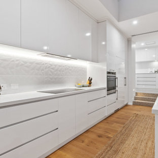 This is an example of a large contemporary l-shaped kitchen in Perth with an undermount sink, flat-panel cabinets, white cabinets, white splashback, panelled appliances, medium hardwood floors, with island, beige floor and white benchtop.