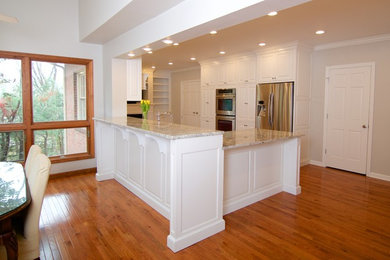 Example of a mid-sized classic u-shaped light wood floor eat-in kitchen design in Other with a farmhouse sink, raised-panel cabinets, white cabinets, granite countertops, white backsplash, subway tile backsplash, stainless steel appliances and a peninsula