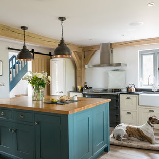 Immagine di una cucina country chiusa con lavello stile country, ante in stile shaker, ante beige, elettrodomestici neri, parquet chiaro, isola e top nero