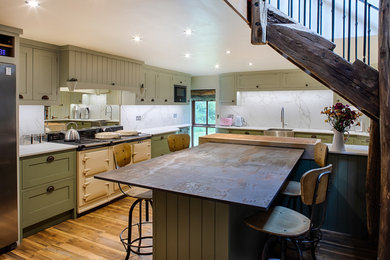 This is an example of a medium sized rural l-shaped kitchen in Other with a belfast sink, shaker cabinets, green cabinets, engineered stone countertops, white splashback, an island, white worktops, marble splashback, light hardwood flooring, coloured appliances and brown floors.