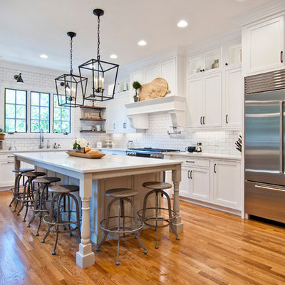 Example of a large cottage l-shaped medium tone wood floor and brown floor kitchen design in Nashville with white cabinets, quartz countertops, white backsplash, subway tile backsplash, stainless steel appliances, an island, white countertops and shaker cabinets