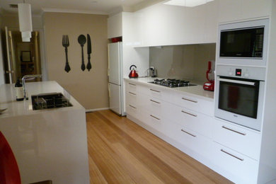 Inspiration för ett mellanstort funkis kök, med en undermonterad diskho, vita skåp, granitbänkskiva, stänkskydd med metallisk yta, glaspanel som stänkskydd, vita vitvaror, ljust trägolv och en köksö