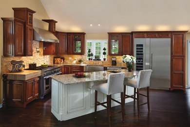 Eat-in kitchen - large transitional l-shaped dark wood floor and brown floor eat-in kitchen idea in Indianapolis with a farmhouse sink, dark wood cabinets, beige backsplash, stainless steel appliances, an island, recessed-panel cabinets, stone tile backsplash, granite countertops and multicolored countertops