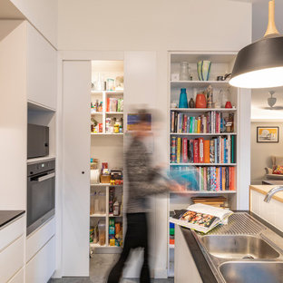 Small scandinavian galley open plan kitchen in Canberra - Queanbeyan with a drop-in sink, flat-panel cabinets, white cabinets, white splashback, ceramic splashback, stainless steel appliances, concrete floors, with island, grey floor and black benchtop.