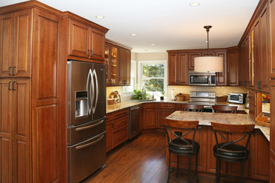 Example of a mid-sized classic u-shaped dark wood floor and brown floor enclosed kitchen design in Baltimore with an undermount sink, raised-panel cabinets, brown cabinets, granite countertops, beige backsplash, glass tile backsplash, stainless steel appliances and an island