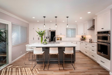 Example of a large transitional l-shaped ceramic tile and brown floor open concept kitchen design in San Francisco with an undermount sink, shaker cabinets, white cabinets, quartz countertops, white backsplash, subway tile backsplash, stainless steel appliances, an island and white countertops