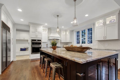 Example of a large transitional u-shaped medium tone wood floor and brown floor eat-in kitchen design in Baltimore with shaker cabinets, white cabinets, white backsplash, subway tile backsplash, stainless steel appliances, an island and a farmhouse sink