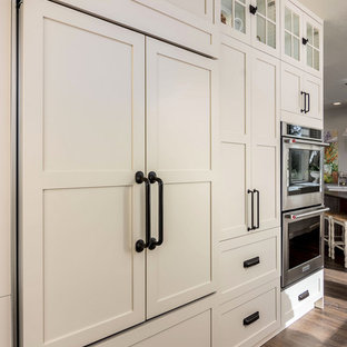 Expansive country galley eat-in kitchen in Portland with a farmhouse sink, shaker cabinets, white cabinets, quartz benchtops, white splashback, stone slab splashback, stainless steel appliances, vinyl floors, with island, brown floor and white benchtop.