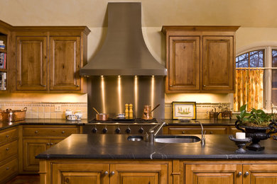 Imagen de cocina clásica con electrodomésticos de acero inoxidable, armarios con rebordes decorativos, puertas de armario de madera oscura, encimera de esteatita y salpicadero beige