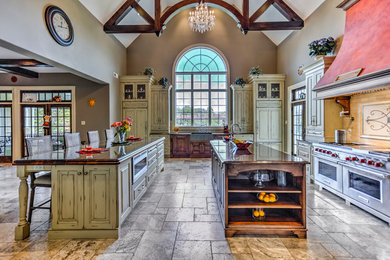 Example of a huge farmhouse galley travertine floor eat-in kitchen design in Philadelphia with a farmhouse sink, raised-panel cabinets, distressed cabinets, granite countertops, beige backsplash, subway tile backsplash, paneled appliances and two islands