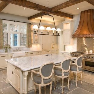 Idee per una cucina a L con lavello stile country, ante con bugna sagomata, ante beige, paraspruzzi a effetto metallico, elettrodomestici in acciaio inossidabile e isola