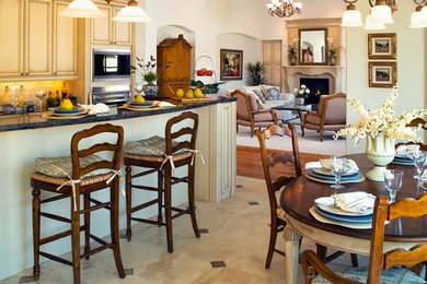 Eat-in kitchen - large traditional u-shaped limestone floor eat-in kitchen idea in Denver with an undermount sink, recessed-panel cabinets, distressed cabinets, soapstone countertops, beige backsplash, stone tile backsplash, stainless steel appliances and an island