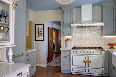 This is an example of a medium sized classic u-shaped kitchen pantry in San Francisco with a belfast sink, beaded cabinets, blue cabinets, engineered stone countertops, beige splashback, terracotta splashback, stainless steel appliances, porcelain flooring, brown floors and beige worktops.