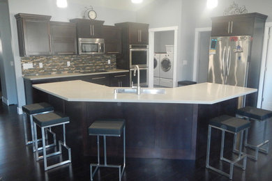 Example of a trendy u-shaped dark wood floor eat-in kitchen design in Other with an undermount sink, recessed-panel cabinets, dark wood cabinets, solid surface countertops, multicolored backsplash, glass tile backsplash, stainless steel appliances and an island