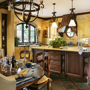 This is an example of a mid-sized traditional l-shaped eat-in kitchen in New York with a farmhouse sink, beaded inset cabinets, yellow cabinets, soapstone benchtops, yellow splashback, mosaic tile splashback, panelled appliances, slate floors, with island and brown floor.