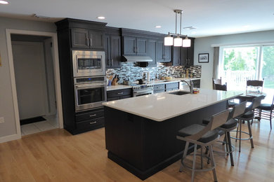 Example of a transitional kitchen design in Bridgeport with stainless steel appliances, an undermount sink, recessed-panel cabinets, quartz countertops, glass tile backsplash and an island