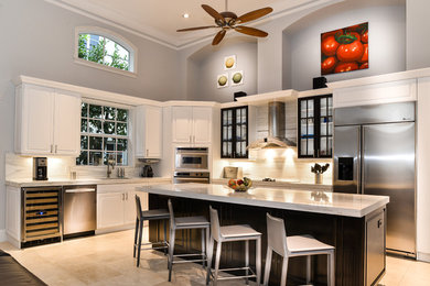 Large traditional l-shaped open plan kitchen in Miami with a submerged sink, shaker cabinets, white cabinets, marble worktops, grey splashback, stone slab splashback, stainless steel appliances, travertine flooring and an island.